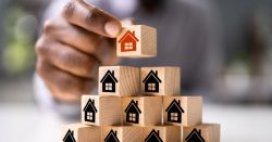 Mano colocando pequeños cubos de madera con dibujos de casas, representando la toma de decisiones en una comunidad de propietarios al cambiar de administrador de fincas