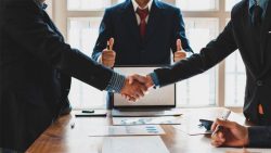 Dos personas estrechándose la mano mientras otra al fondo levanta los pulgares en señal de acuerdo, simbolizando la mediación obligatoria en procesos civiles y mercantiles