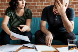 Hombre y mujer sentados en un sofá con expresión de preocupación, con documentos sobre la mesa, ilustrando la gestión de morosidad en la comunidad de propietarios
